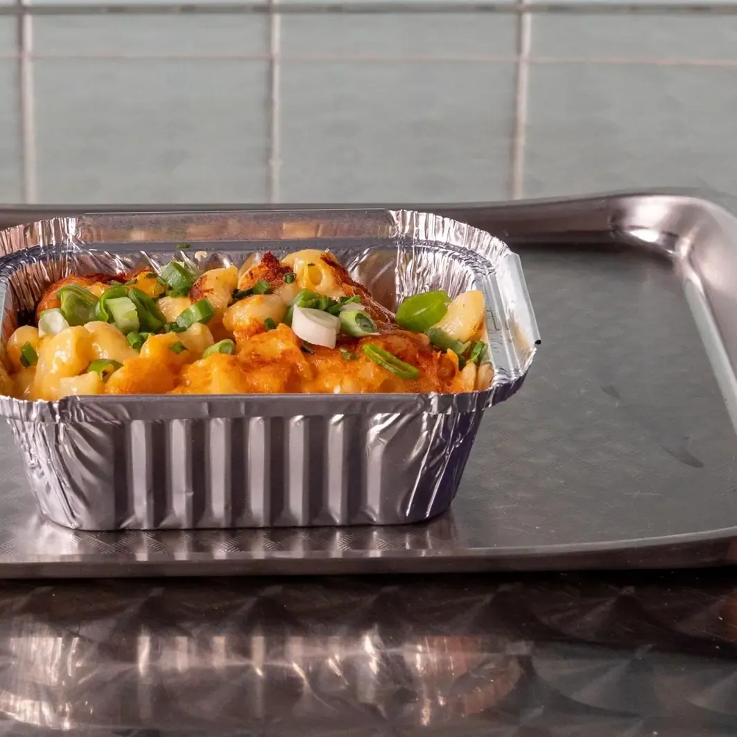 Mac & cheese servido en una bandeja de acero sobre papel a cuadros